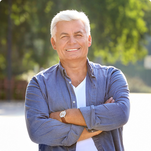 Older man smiling outside with arms folded
