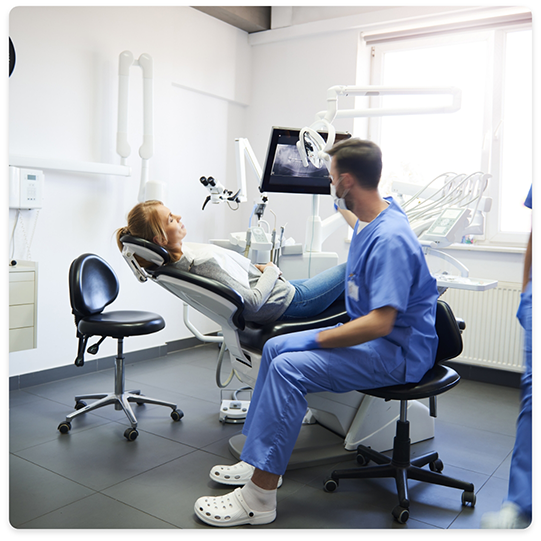 Woman in dental chair talking to dentist sitting nearby