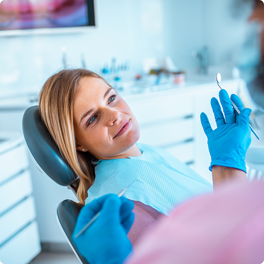 Blonde woman in dental chair looking at a dentist holding a dental mirror
