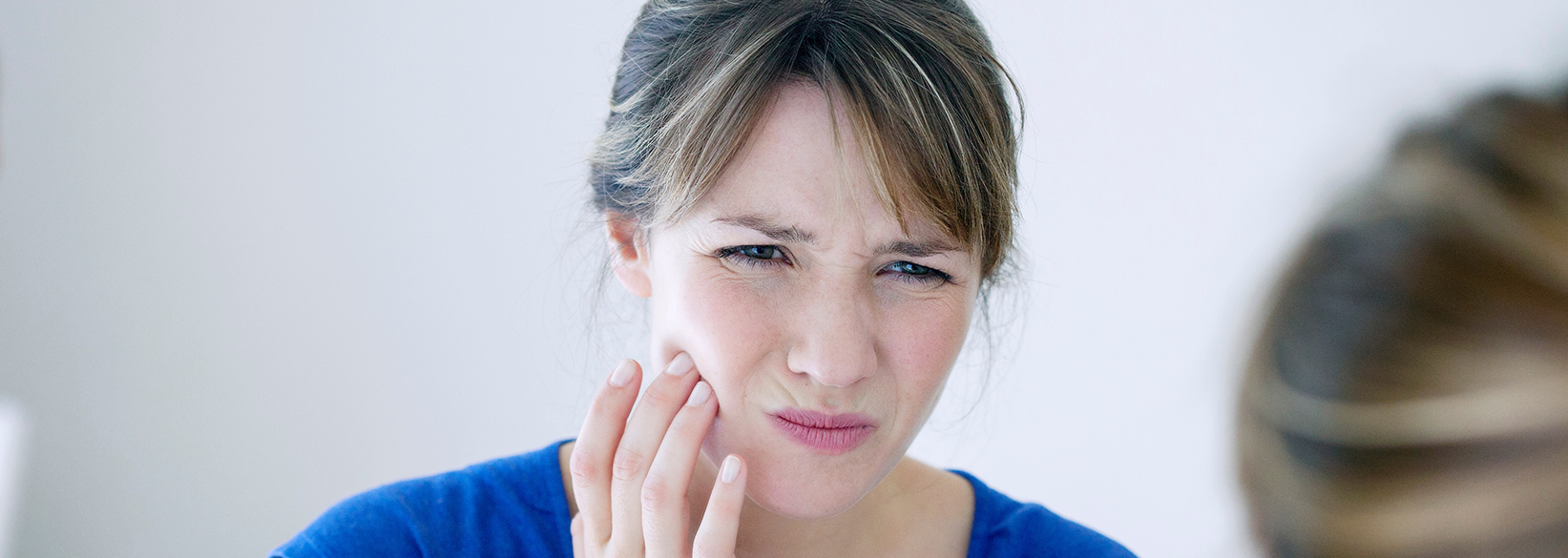 Woman rubbing the side of her jaw in pain before seeing an emergency dentist in Fredericksburg