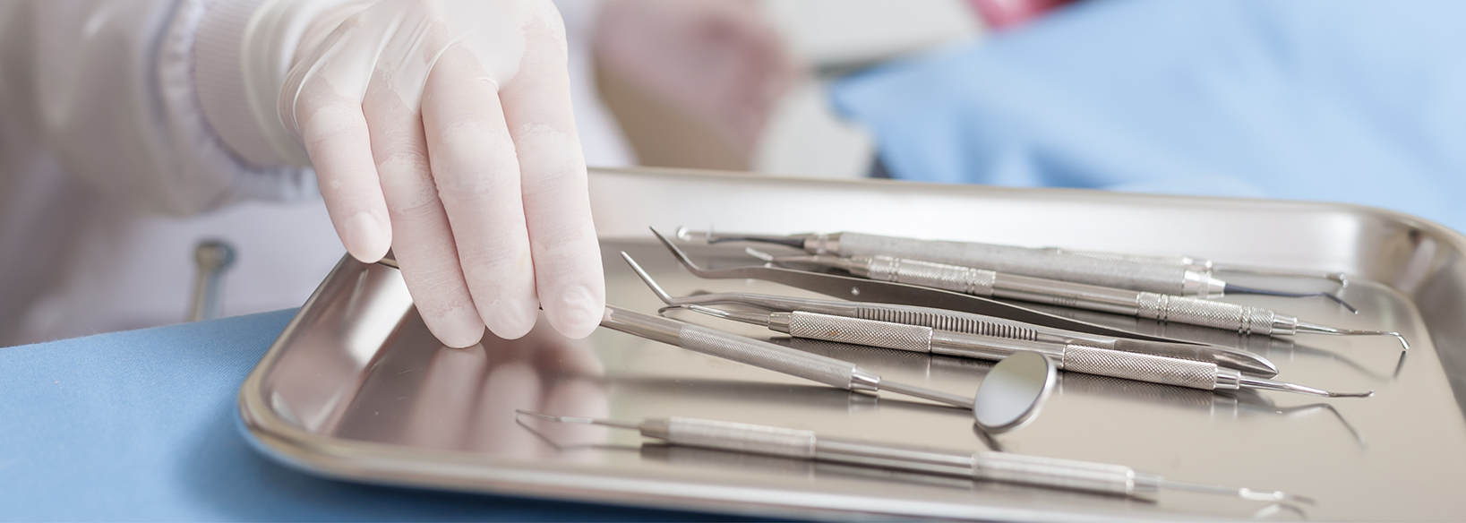 Gloved hand picking up dental instruments in tray